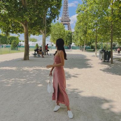 Lee is wearing a pink dress and white sneakers while looking at Eiffel Tower behind her.
